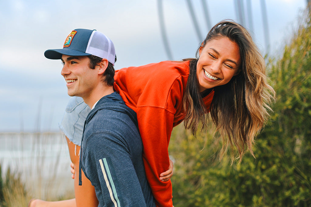 Photo of a guy holding a girl on his shoulder at the beach, they're both smiling. Everyday California Sale Section.