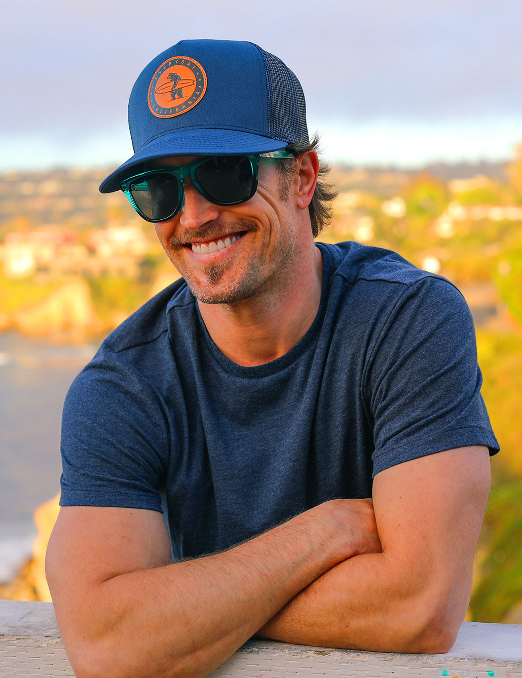 Photo of a man wearing a hat and sunglasses smiling at the camera.